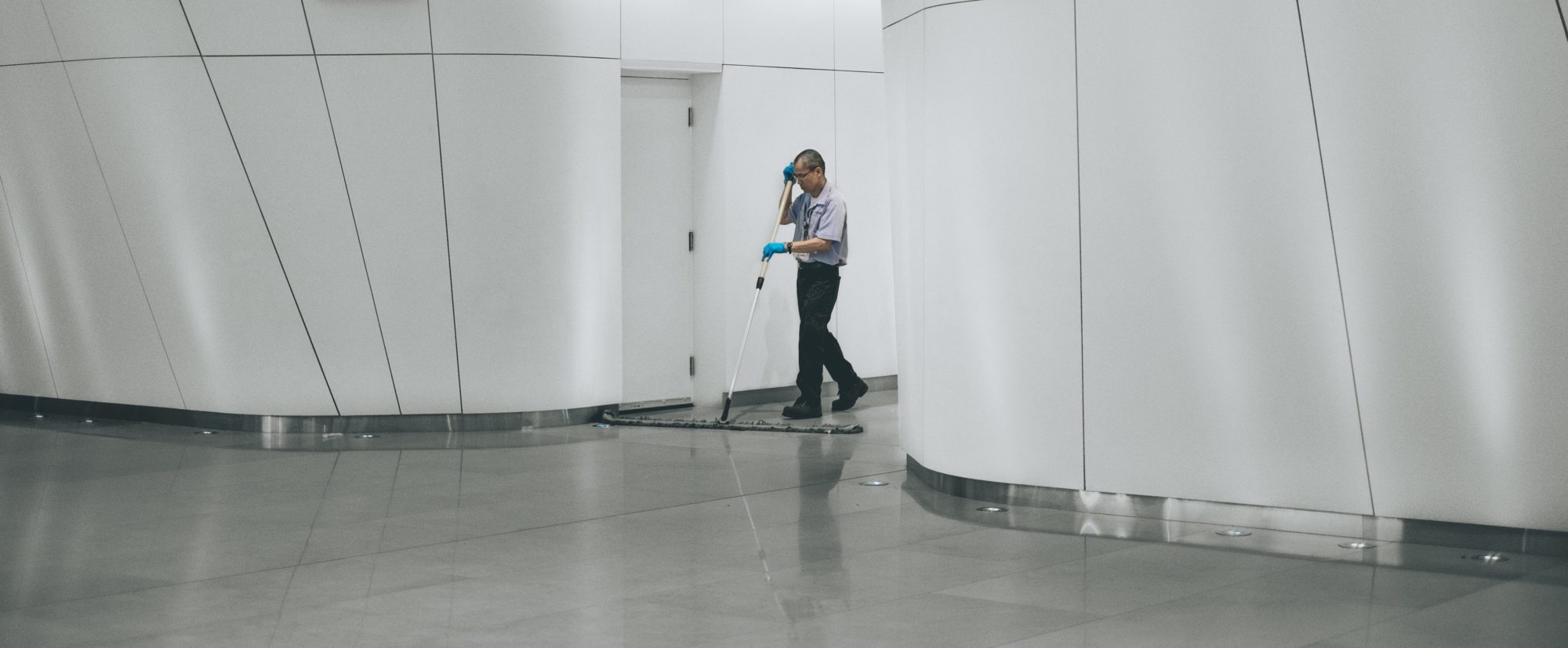 employé nettoyant le sol avec une grande serpilière dans un hall d'immeuble de bureaux et de locaux professionnels / Worker cleaning floor